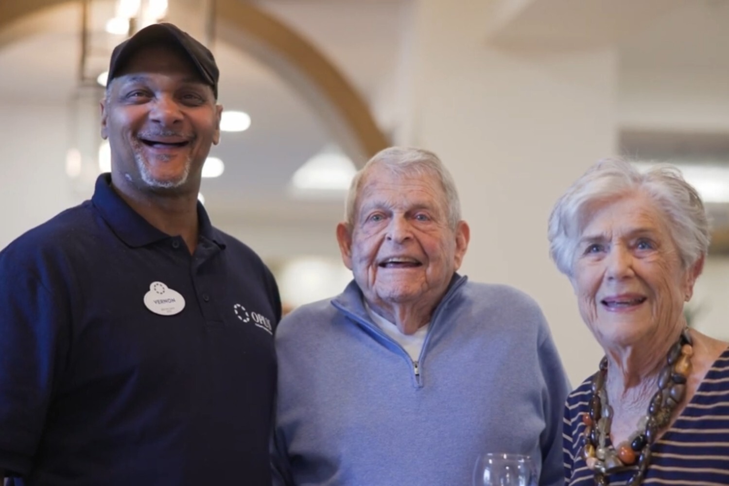 A staff member smiles alongside two residents in the elegant common area at Opus East Memphis, reflecting the warm, personalized connections that define senior living in East Memphis, TN.