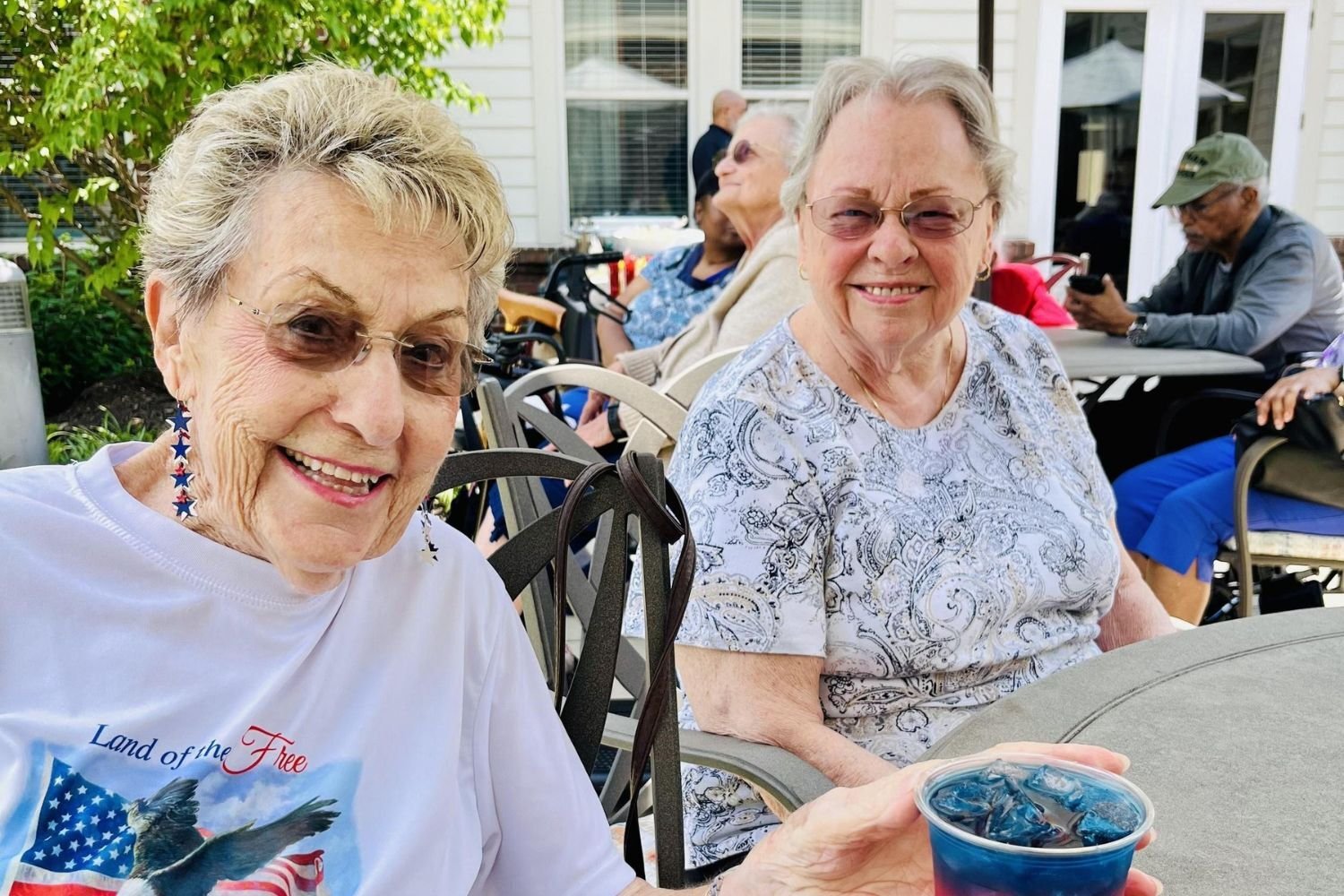 women/residents smile and drink blue liquid while sitting at a table outside