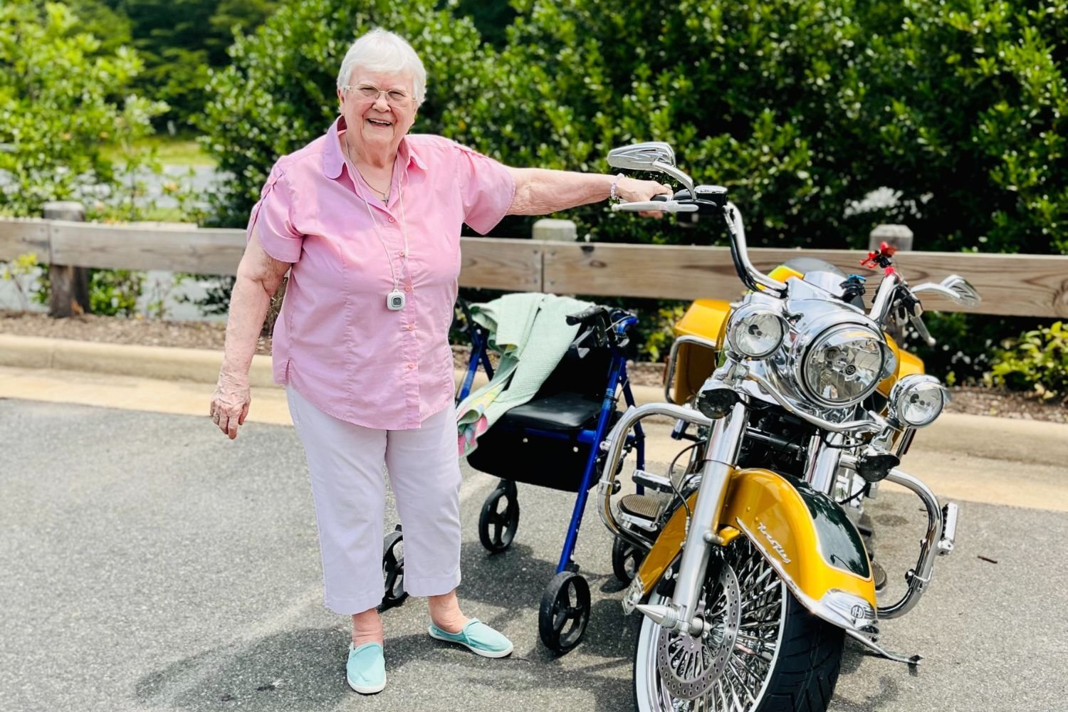woman/resident wears a pink shirt and stands by a yellow motorcycle outside