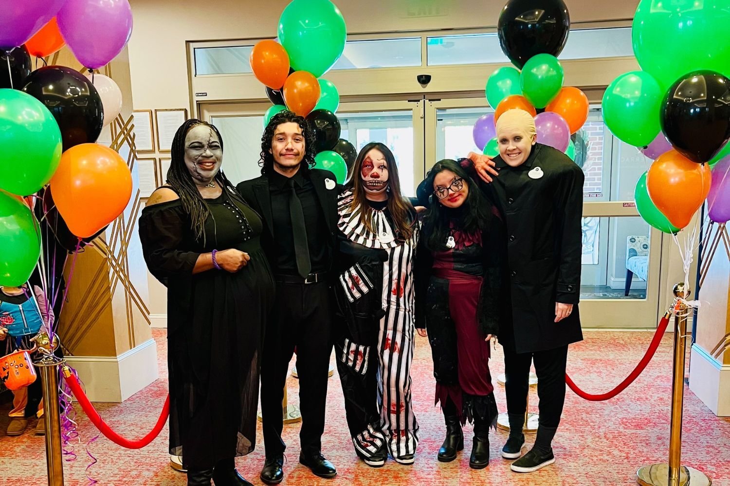 employees stand in their Halloween costumes with their arms wrapped around each other