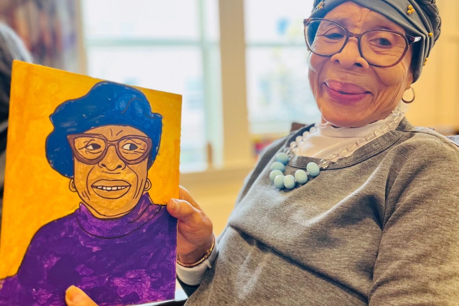 woman with glasses smiles holding a self portrait