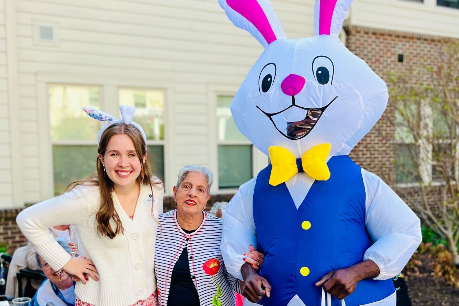 two women stand next to a man dressed as the easter bunny. One woman has bunny ears on