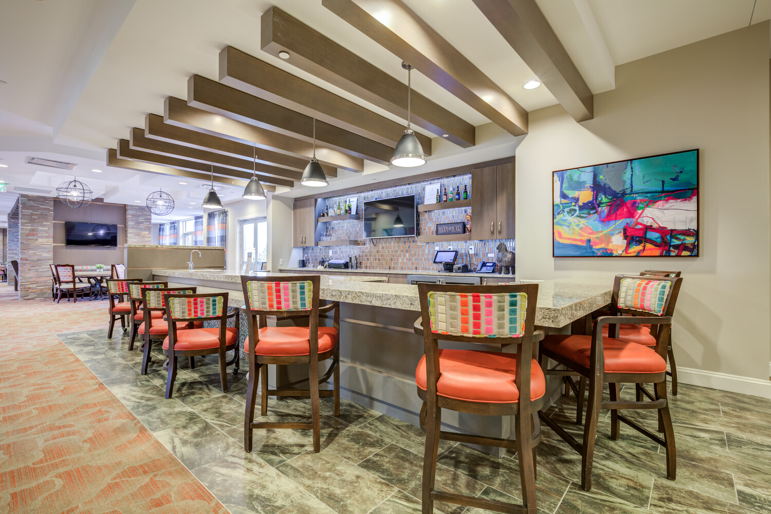 Stylish bar and lounge area at Arbor Terrace Prince William Commons with colorful seating and vibrant artwork, part of the active senior community in Prince William County.