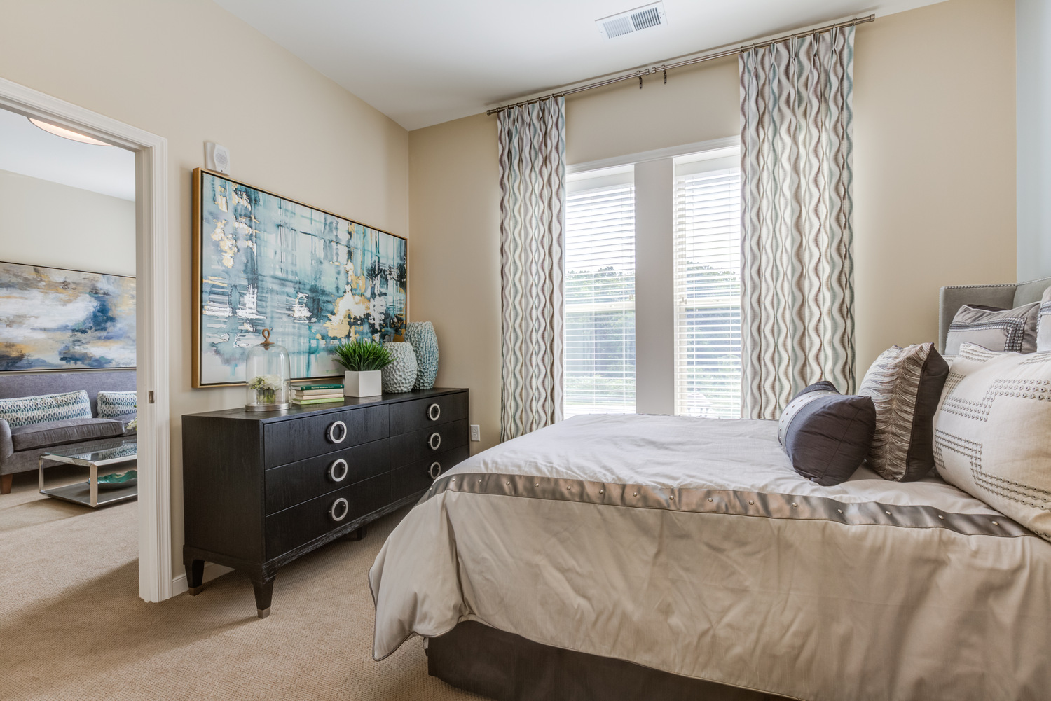 Sunlit bedroom at Arbor Terrace Prince William Commons with patterned drapery, a sleek dresser, and plush bedding, part of comfortable senior housing in Woodbridge VA.