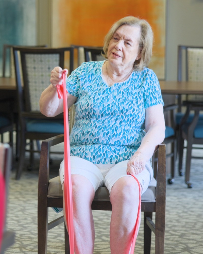A resident uses a resistance band during a seated exercise session, reflecting the wellness-focused senior living Northern Virginia programs offered as part of this active senior community Prince William County lifestyle.