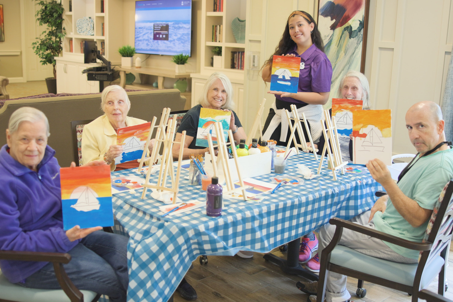 Residents and a staff member enjoy a lively painting class together, showcasing colorful artwork and creative expression as part of the engaging 55+ senior living Woodbridge lifestyle near Prince William Forest Park.