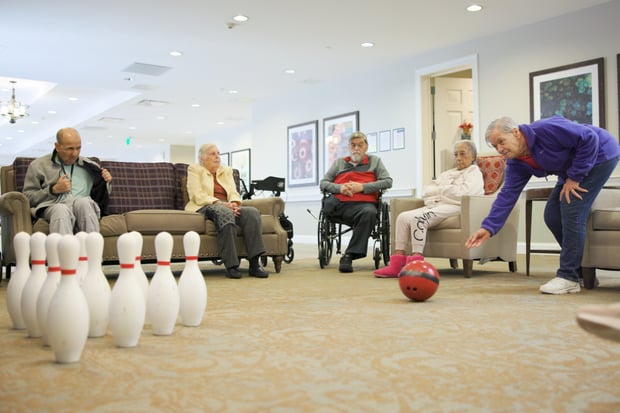 Residents gather in a cozy lounge to enjoy a friendly bowling game with bright pins and a red ball, reflecting the connected, engaged lifestyle found at this active senior community Prince William County within senior living Woodbridge VA.