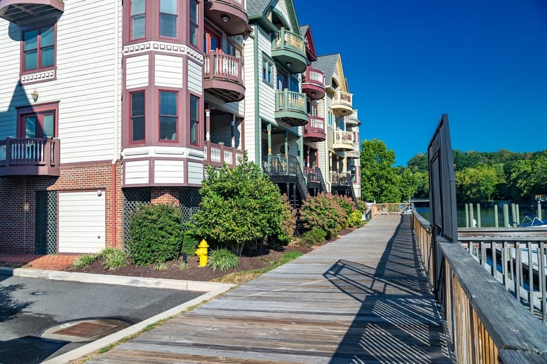 Colorful waterfront rowhouses line a boardwalk under a bright blue sky, showcasing the charming hometown scenery of senior living Woodbridge VA, part of the vibrant 55+ senior living Woodbridge community.