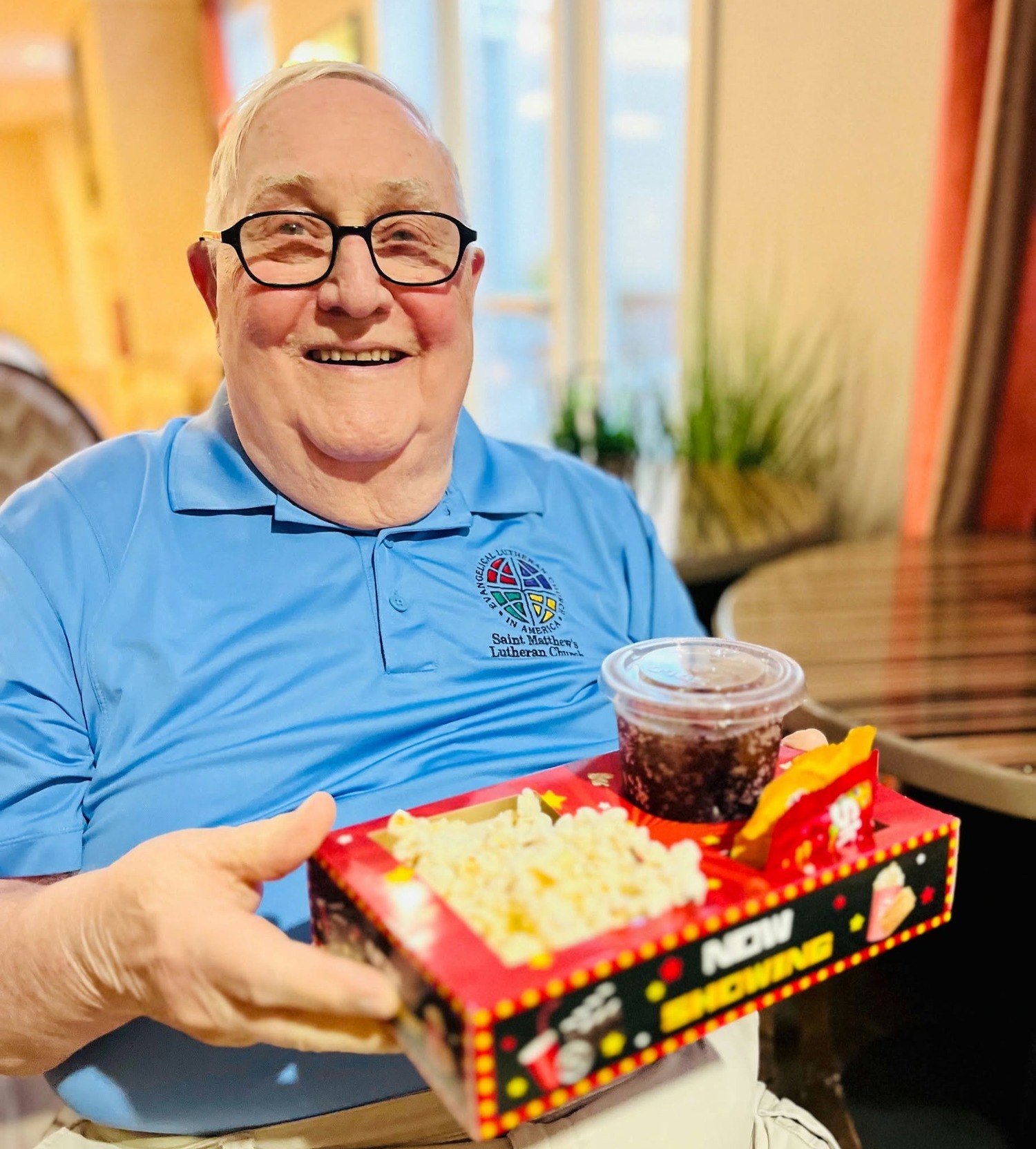 A resident smiles while holding a movie night snack tray with popcorn, candy, and a drink, capturing a fun entertainment tradition within this active senior community Prince William County and senior living Woodbridge VA.