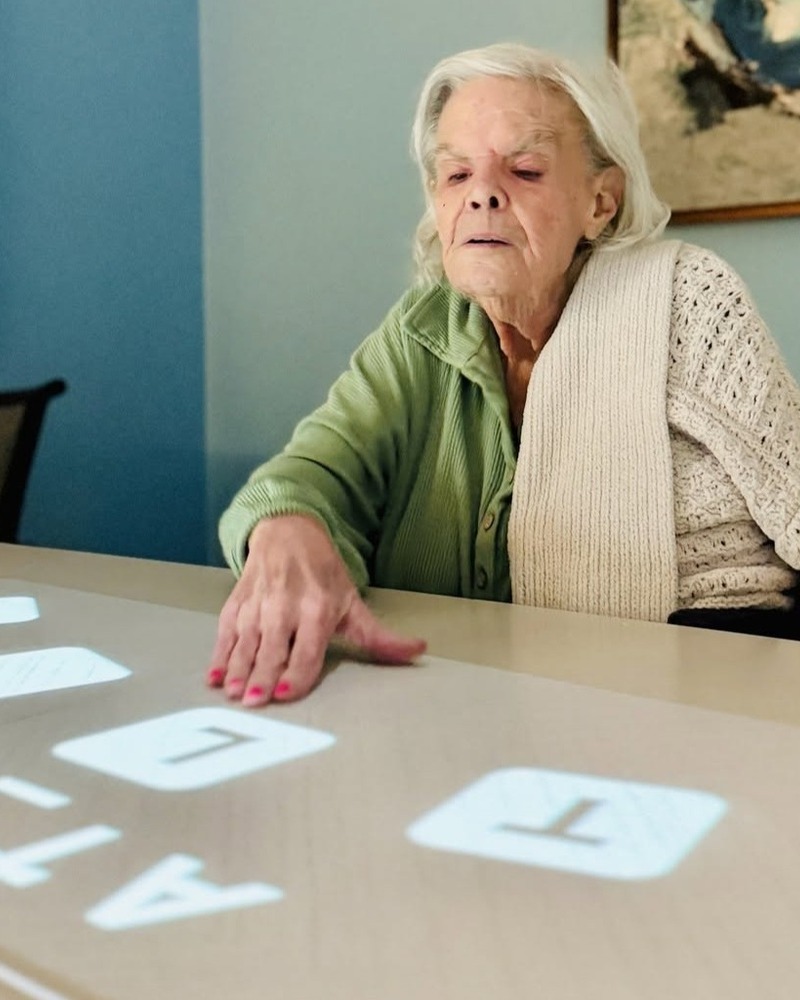 A resident reaches for large letter tiles spread across a table, enjoying a word game that reflects the engaging, wellness-focused senior living Northern Virginia lifestyle at this community.