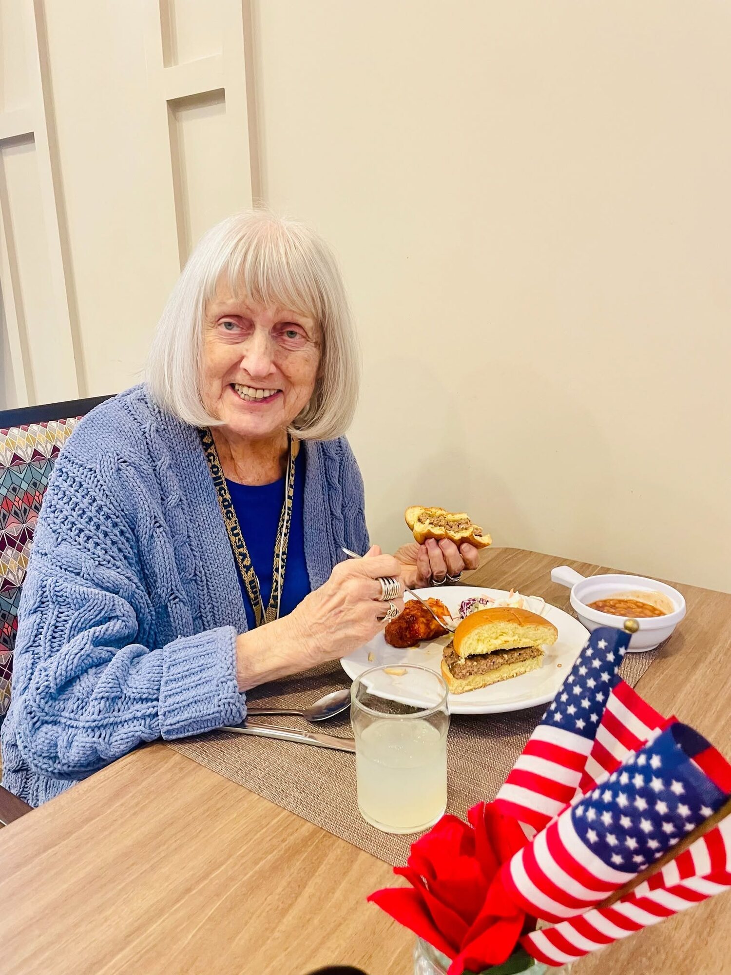 A resident enjoys a hearty meal of soup and a sandwich at a table decorated with small American flags, capturing a festive dining moment that reflects the resort-style senior living Woodbridge hospitality and wellness-focused senior living Northern Virginia lifestyle.