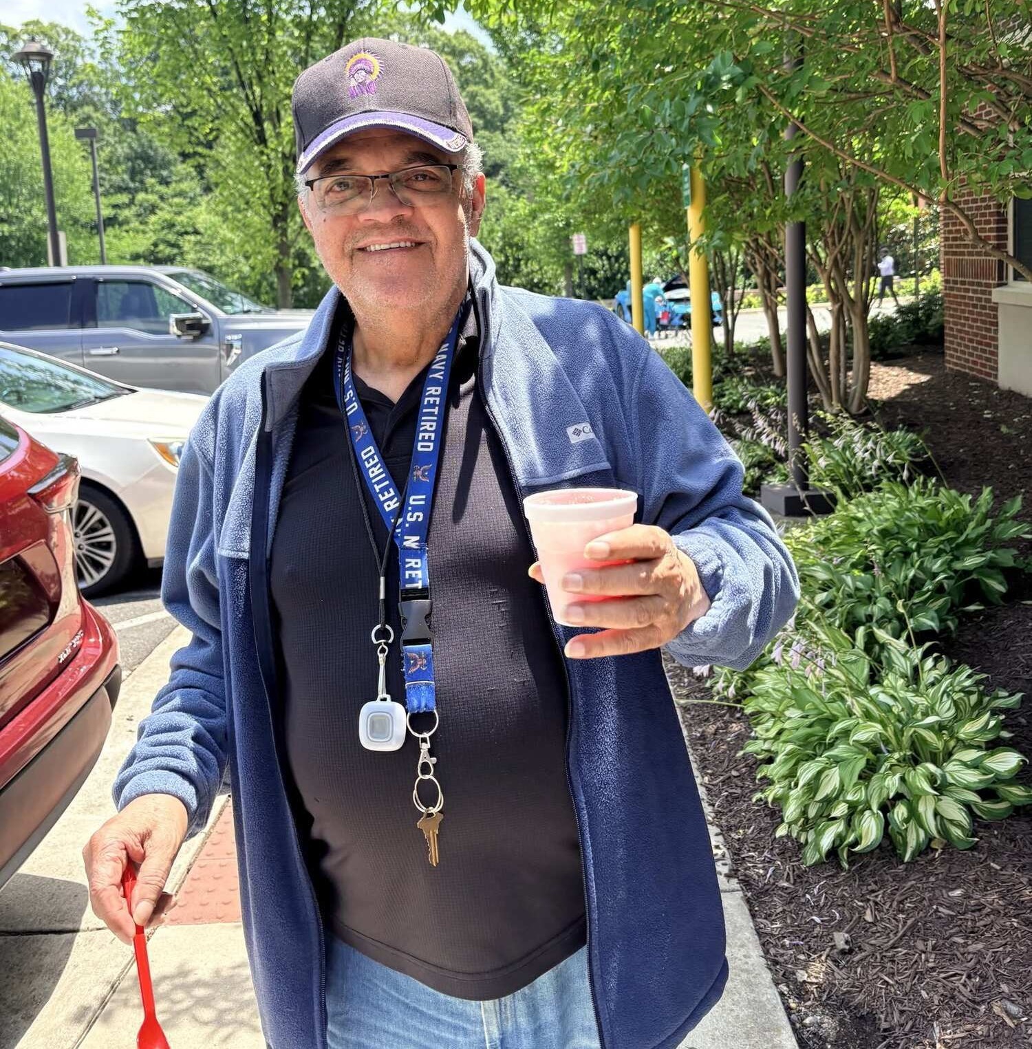 A resident smiles while holding a refreshing drink outside on a sunny day, enjoying the walkable senior living Woodbridge VA setting and easy access that makes senior living near Potomac Mills so convenient for residents.