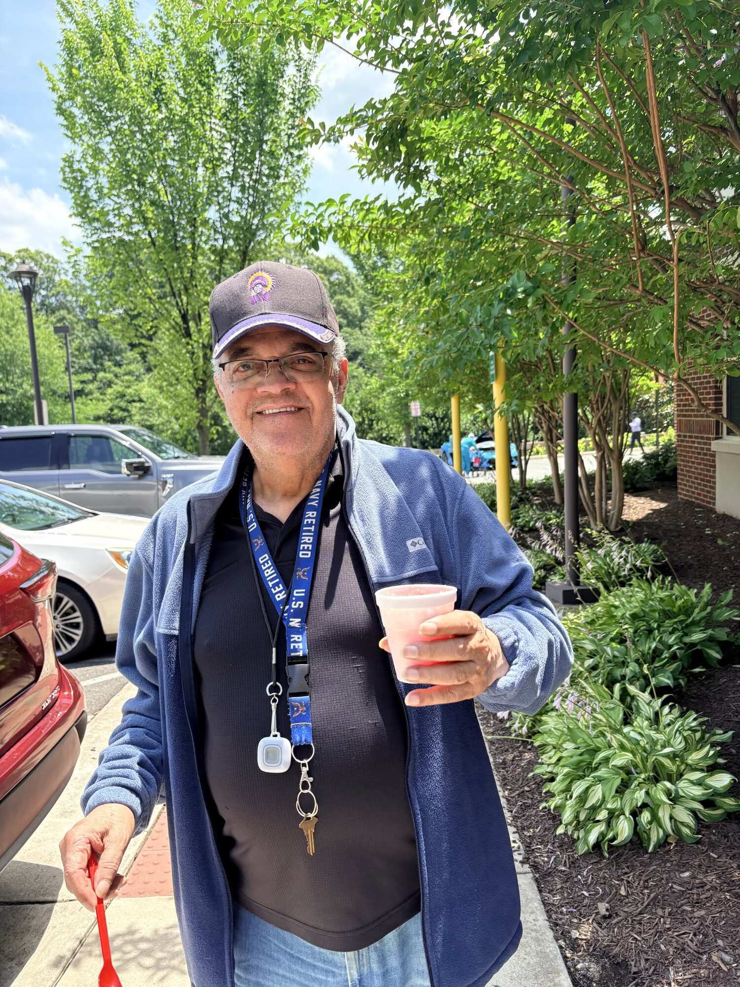 A resident smiles while holding a refreshing drink outside on a sunny day, enjoying the walkable senior living Woodbridge VA setting and easy access that makes senior living near Potomac Mills so convenient for residents.
