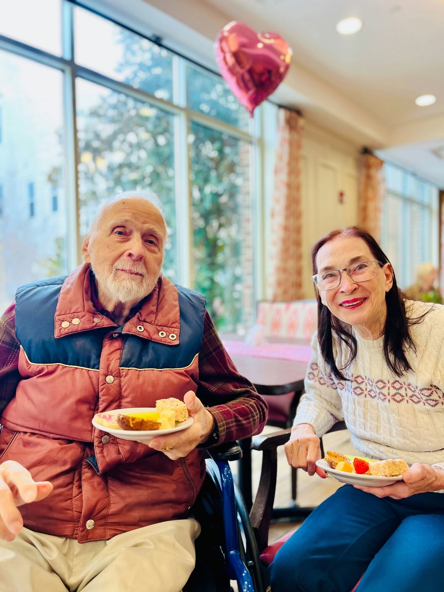 Two residents share a joyful moment over dessert at a festive Valentine's gathering, reflecting the vibrant senior living near Potomac Mills community and warm senior living Woodbridge VA atmosphere residents enjoy.