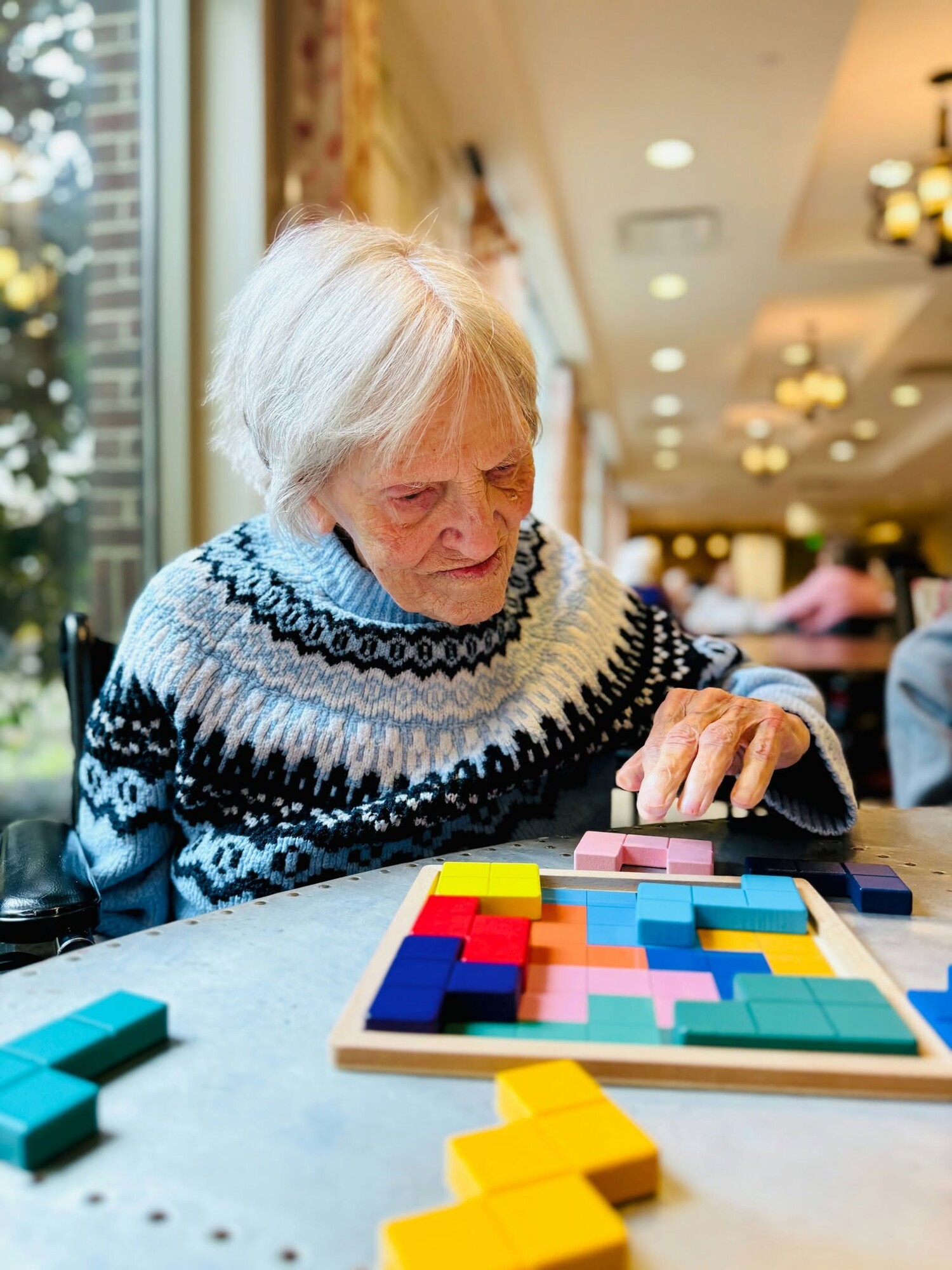 A resident carefully arranges colorful puzzle pieces at a table, enjoying an engaging brain game that reflects the vibrant senior living Woodbridge VA lifestyle found within this 55+ senior living Woodbridge community.