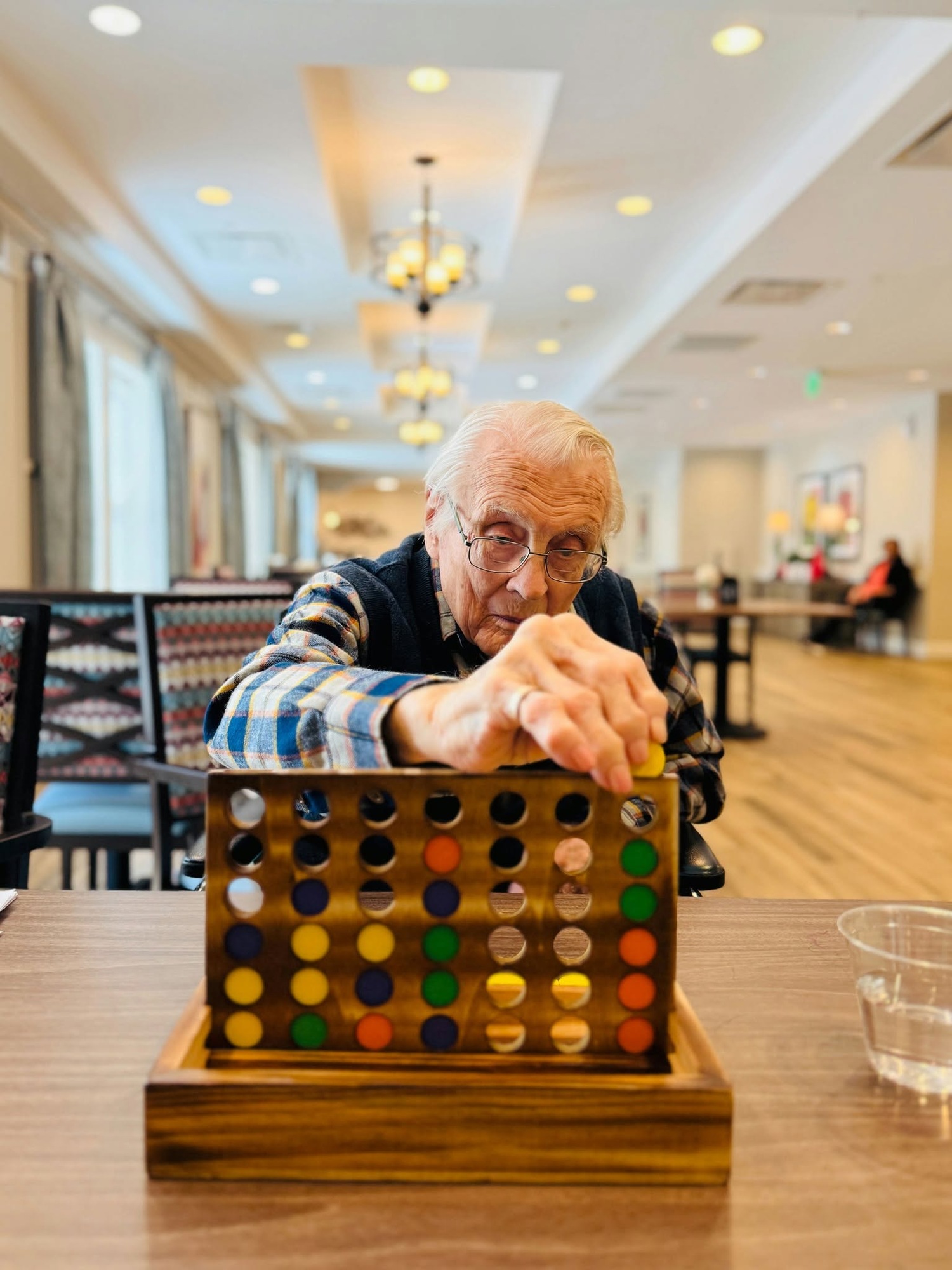 A resident carefully places a game piece into a colorful Connect Four board in a bright hallway, reflecting the engaging, active senior community Prince William County lifestyle at senior living Woodbridge VA.