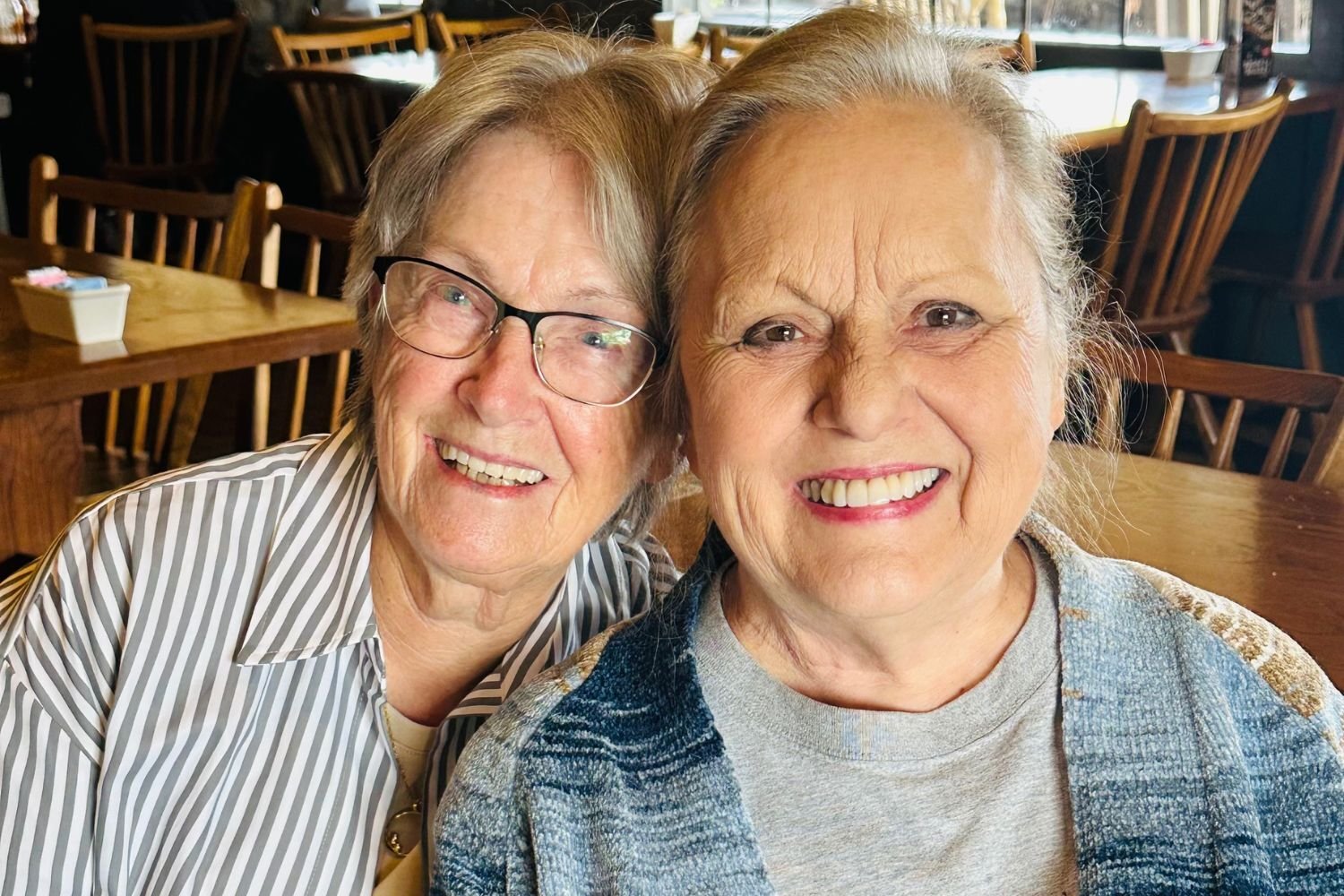 two women lean on each other while sitting and smiling