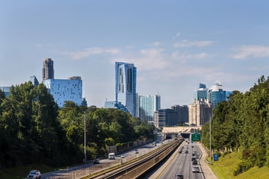 A view of the Atlanta skyline rises above a tree-lined highway, capturing the vibrant surroundings near senior living in Sandy Springs, GA and North Atlanta, GA.
