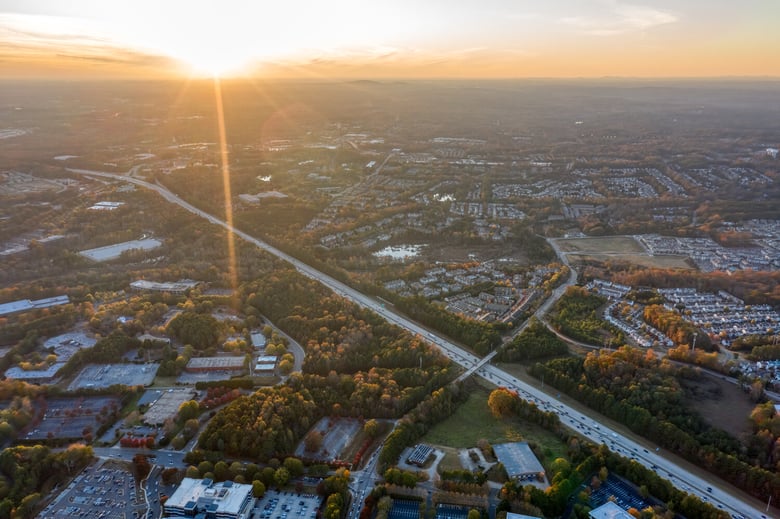 A golden sunset illuminates a sprawling suburban landscape and winding roadways, capturing the scenic senior living near Roswell, GA and Sandy Springs, GA.