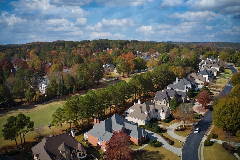 An aerial view showcases a leafy suburban neighborhood with autumn colors and rooftops, capturing the charm of senior living in Sandy Springs, GA and North Atlanta, GA.