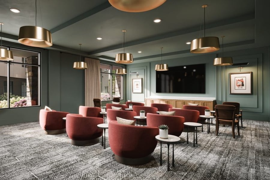 A cozy theater-style lounge with plush burgundy chairs, gold pendant lighting and a wall-mounted TV, showcasing engaging senior lifestyle programs Sandy Springs residents enjoy as part of the resort-style senior amenities in Sandy Springs.