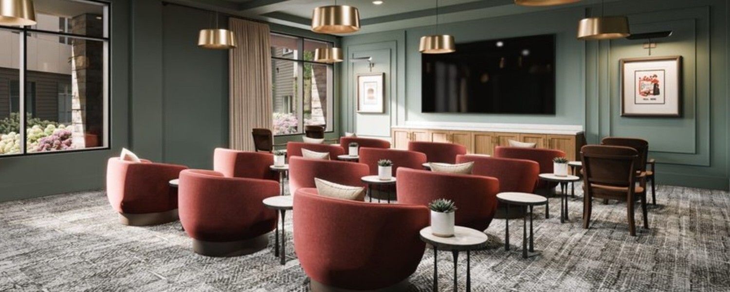 A stylish media lounge features plush red curved chairs, a large screen, and elegant sconce lighting, showcasing the engaging senior lifestyle programs near Sandy Springs, GA and Buckhead, GA.