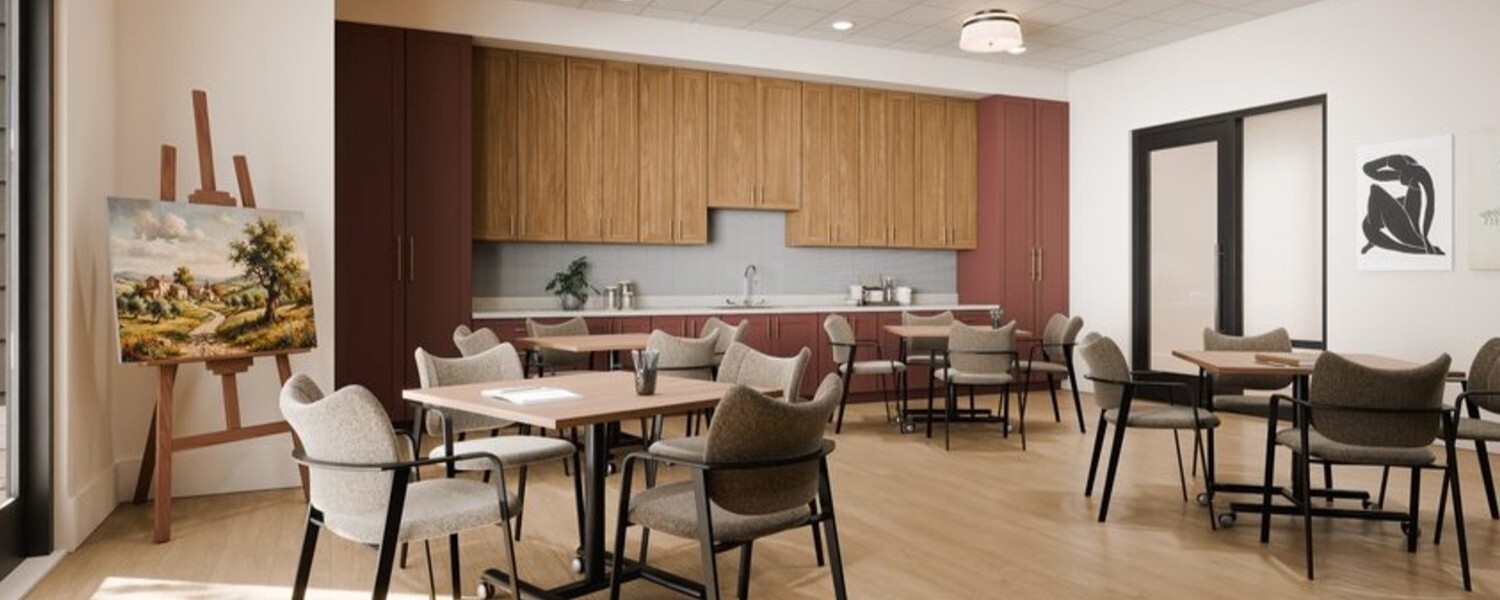 A bright dining and activity space features an easel with a painted canvas, warm wood cabinetry, and communal seating, showcasing the chef-prepared dining senior living in Sandy Springs, GA offers near Perimeter, GA.