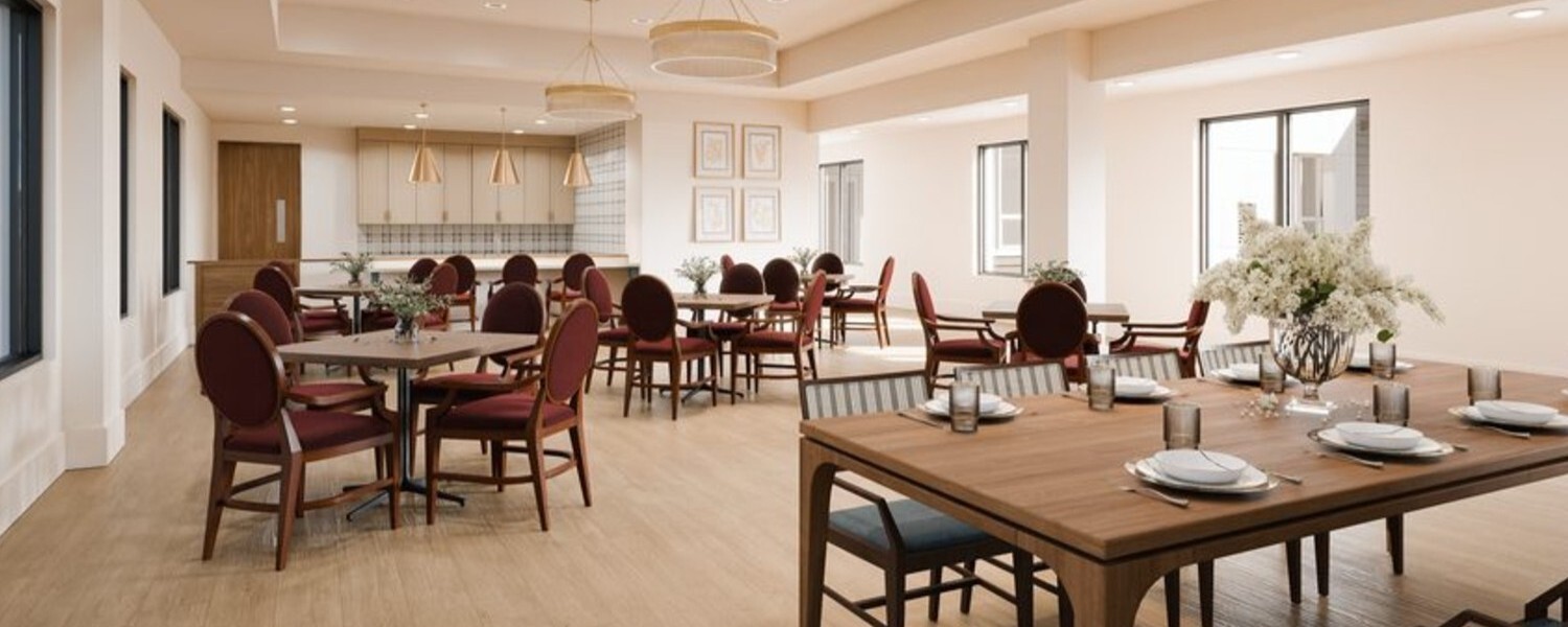 An elegant dining room features neatly set tables, upholstered chairs, and warm pendant lighting bathed in natural light, showcasing the chef-prepared dining senior living in Sandy Springs, GA offers.