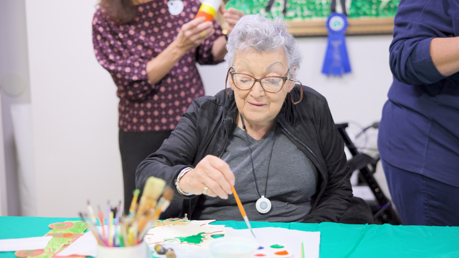 A resident smiles while working on an art project at Arbor Terrace Shrewsbury, surrounded by colorful supplies — a warm moment from daily enrichment in senior living Tinton Falls NJ.