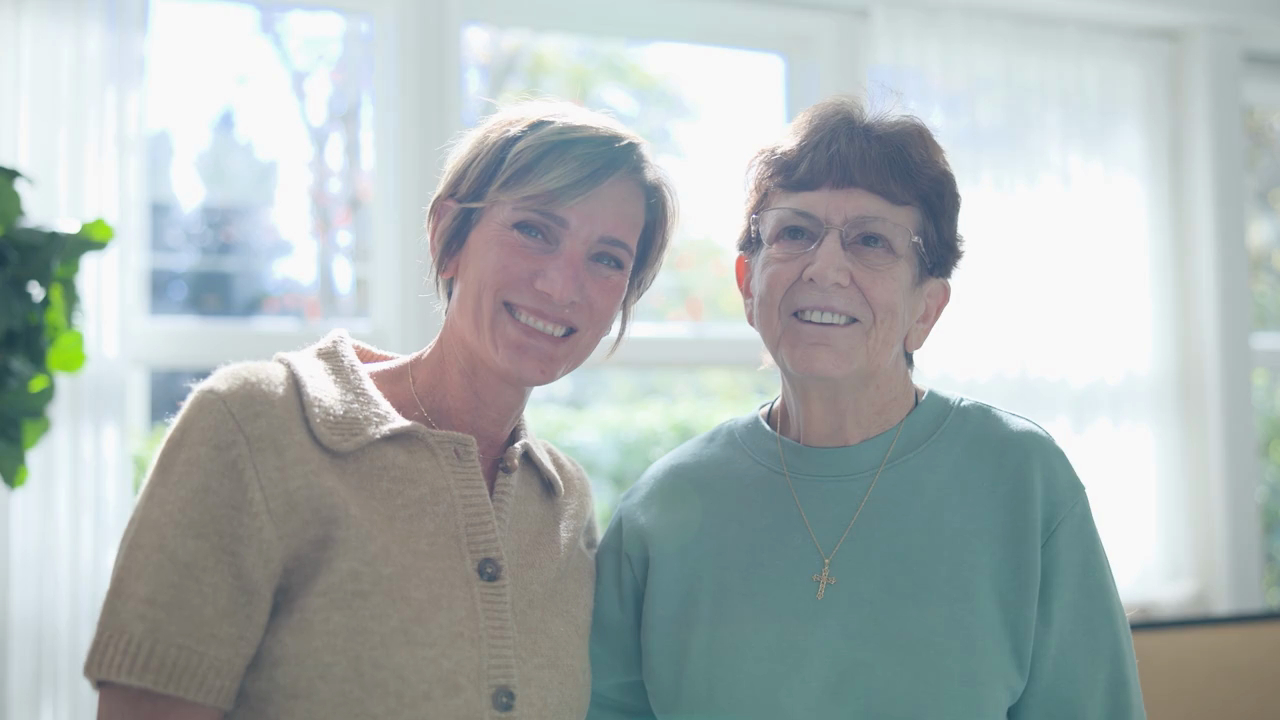 A senior lady and her adult daughter taking a photo by the window with wide smiles