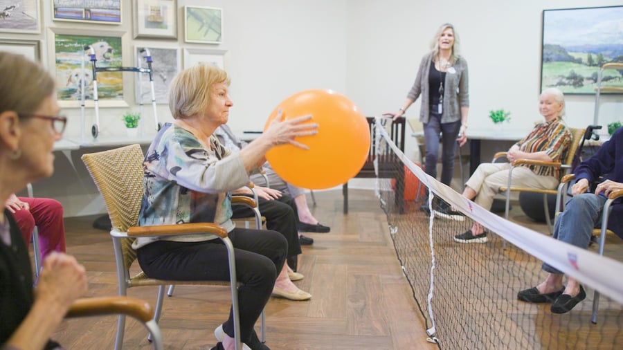 Residents engage in a lively balloon activity led by a staff member in a bright common room, highlighting the wellness-focused senior living experience at Arbor Terrace South Forsyth in Suwanee, GA.