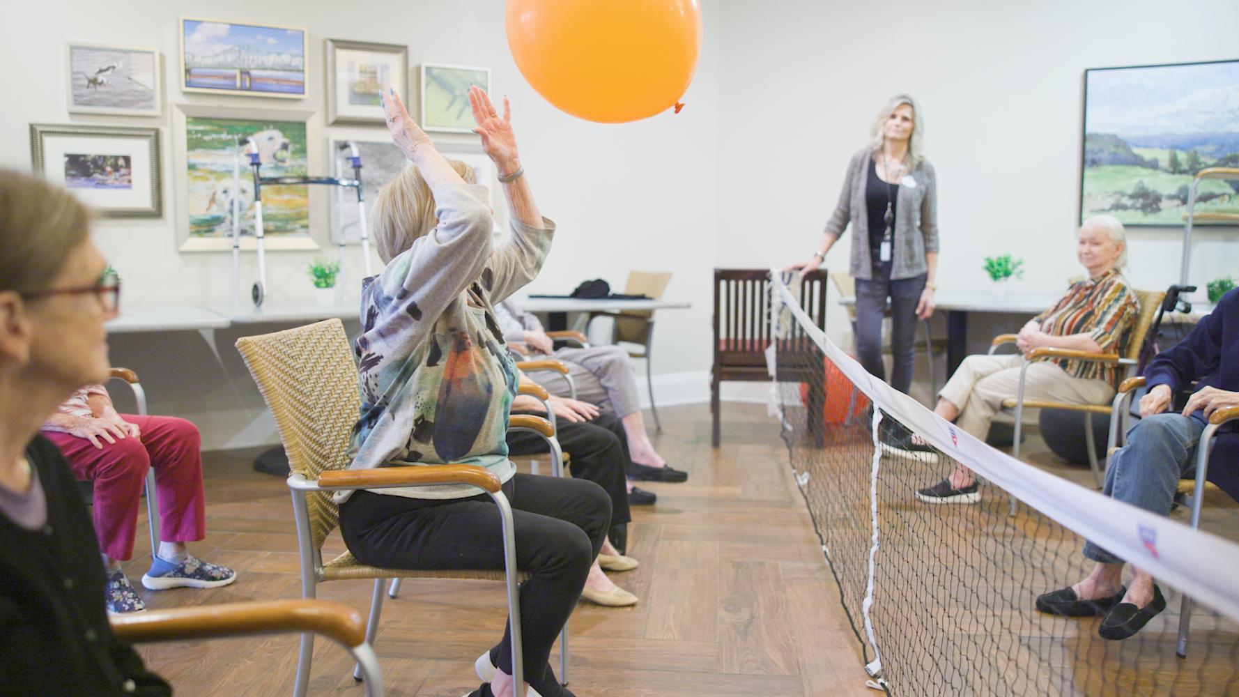 A staff member leads residents in a ribbon and balloon activity, bringing energy and fun to the common area at this South Forsyth senior living community.