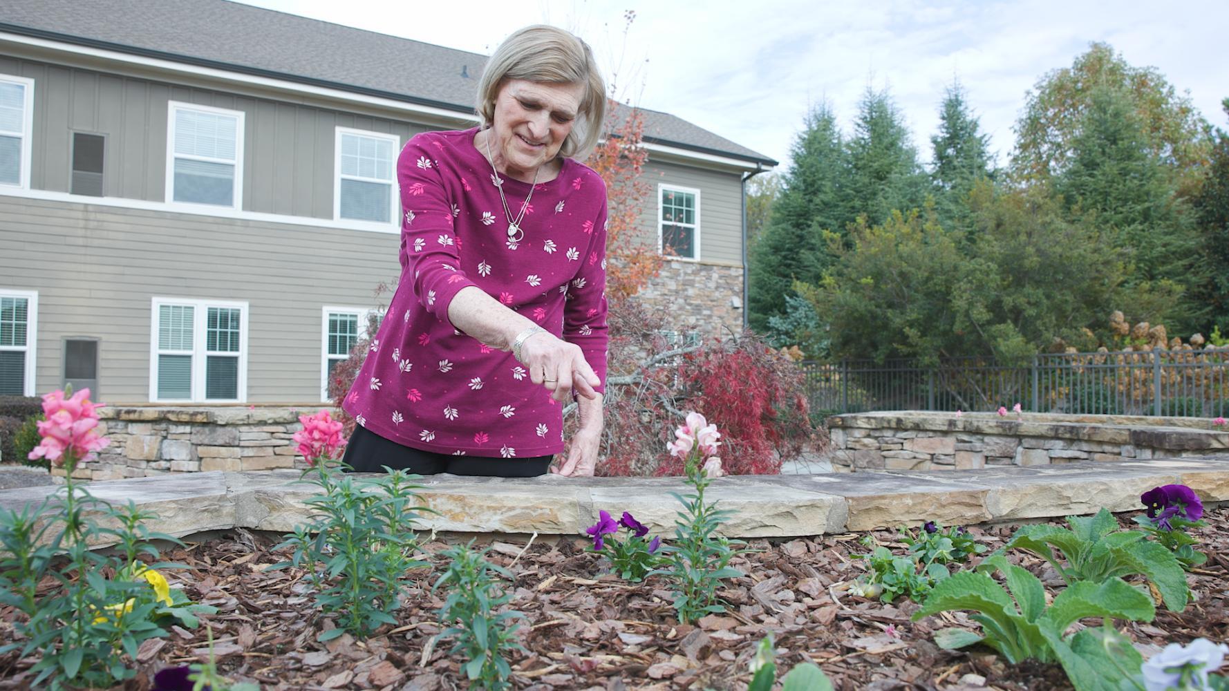 A person kneels among blooming flowers in a well-kept garden at Arbor Terrace South Forsyth, reflecting the community's warm, nature-inspired setting.