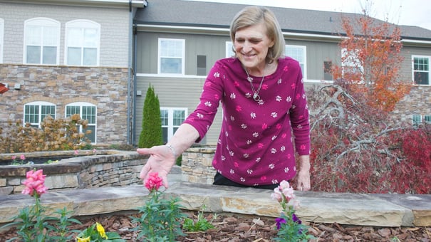 A person smiles while tending to blooming flowers in the beautifully maintained garden at Arbor Terrace South Forsyth, a trusted memory care community in Suwanee, GA.