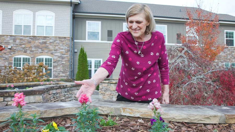 A person smiles while tending to blooming flowers in the beautifully maintained garden at Arbor Terrace South Forsyth, a trusted memory care community in Suwanee, GA.
