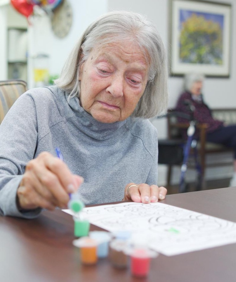 An older woman focuses intently on a painting activity at Arbor Terrace South Forsyth, showcasing the creative arts programming that enriches daily life for senior living in Suwanee, GA.