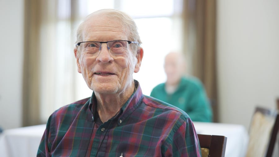 A resident smiles warmly while seated in a bright dining area at Arbor Terrace South Forsyth, a welcoming senior living community in Suwanee, GA.