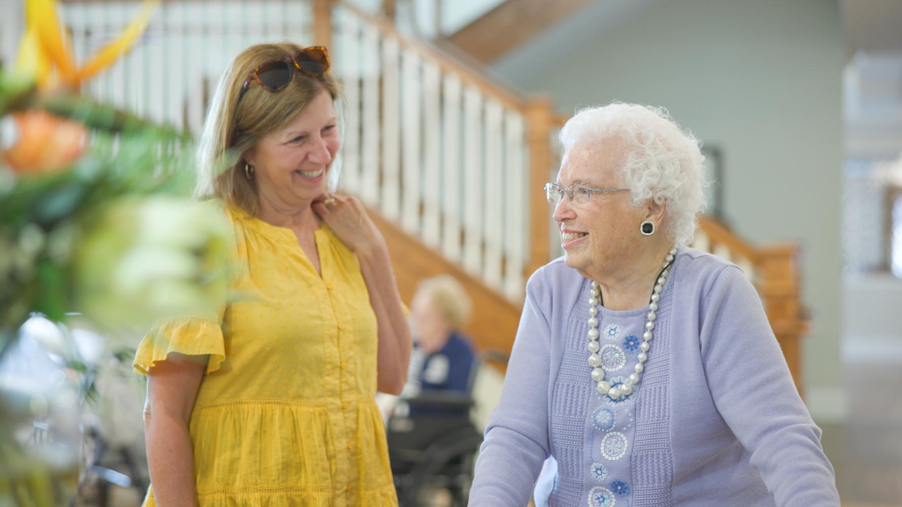 A resident and a visitor share a cheerful conversation near a bright staircase inside this assisted living community in Suwanee, GA, enjoying a warm and welcoming atmosphere together.