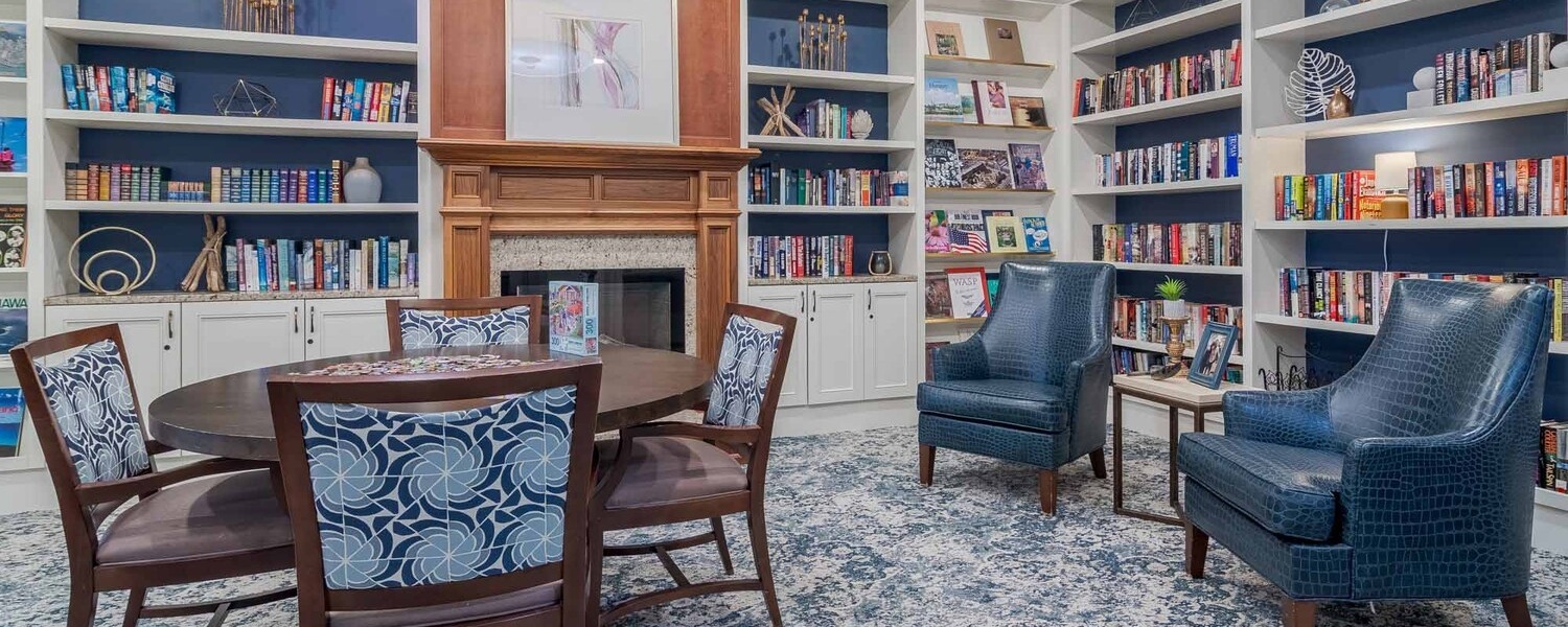 A cozy library and sitting room at Arbor Terrace South Forsyth features built-in bookshelves, a fireplace, and comfortable seating, offering a peaceful retreat for residents of this senior living community in Suwanee, GA.