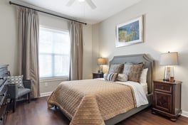 A tastefully furnished apartment bedroom with warm tones, soft bedding, and natural light at this senior living community in South Forsyth.