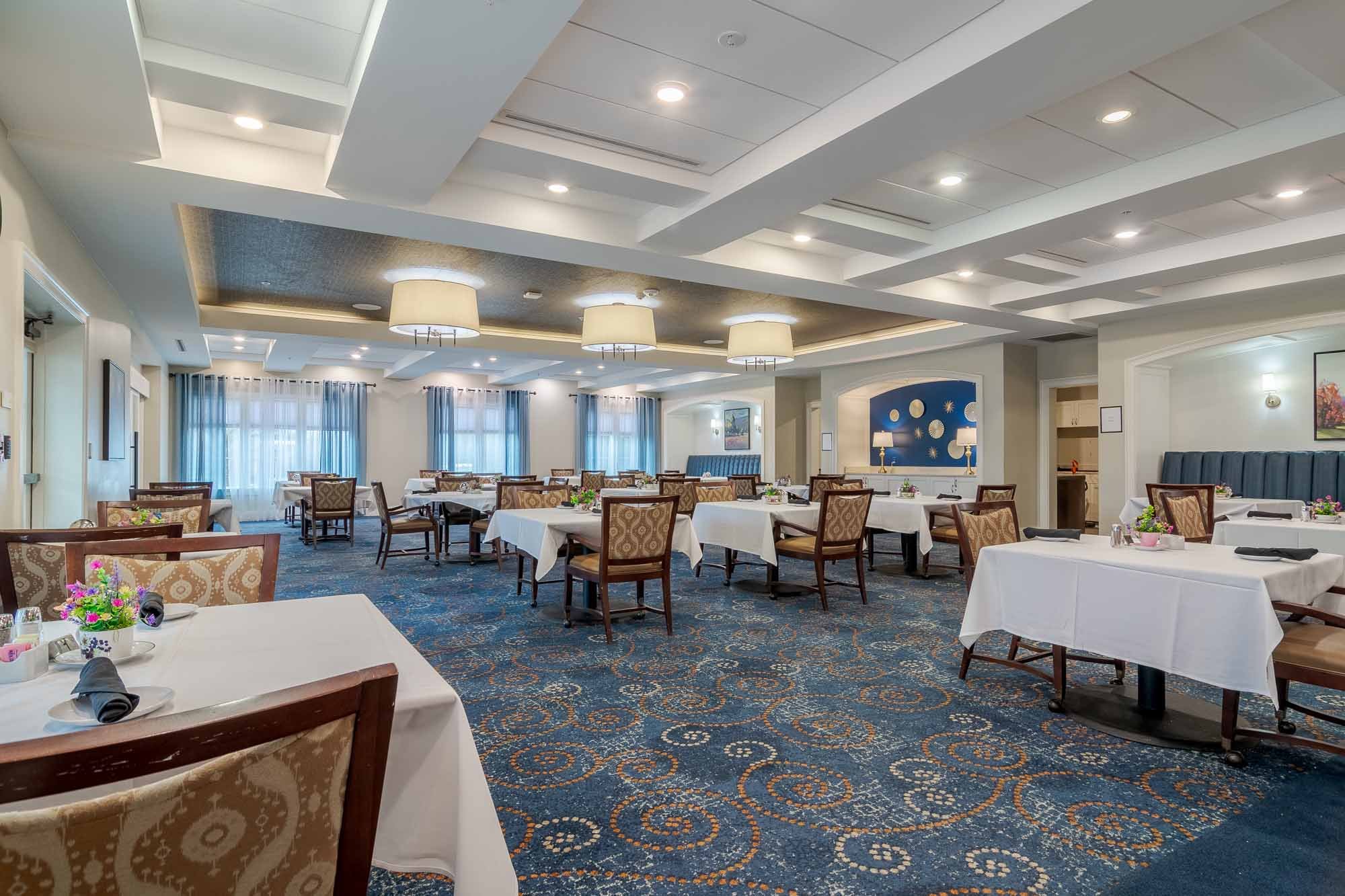 A large, elegantly appointed dining room with white-draped tables and warm overhead lighting at Arbor Terrace South Forsyth assisted living.
