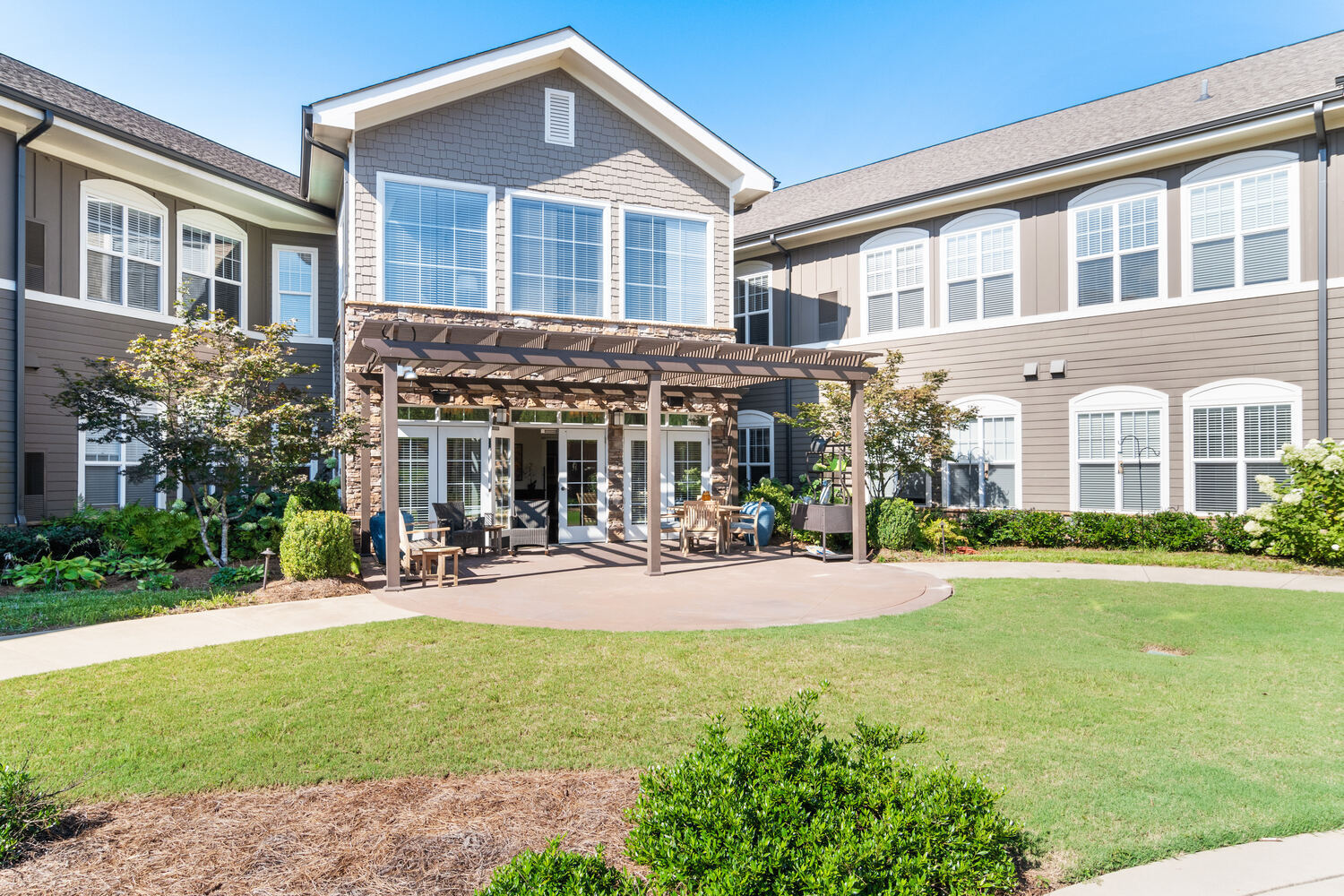 A lush, well-maintained patio and courtyard area with manicured grounds and a pergola at Arbor Terrace, a nature-focused senior living community in South Forsyth