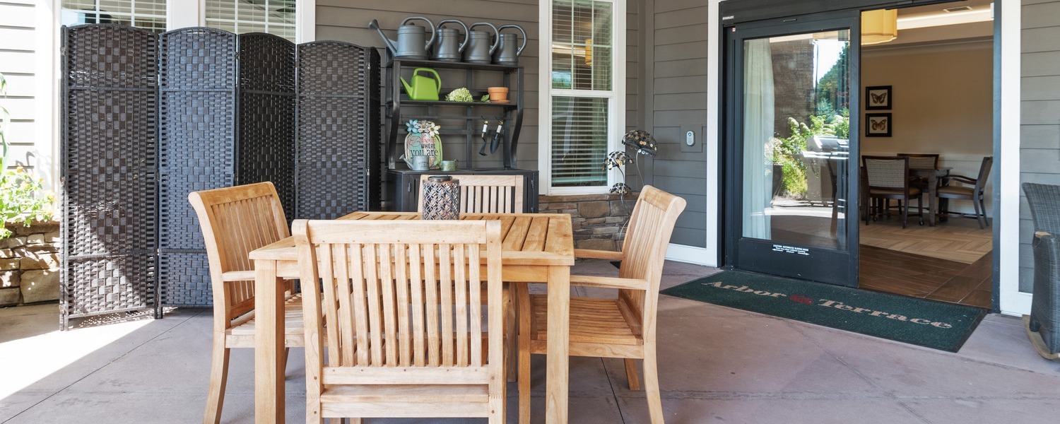 Inviting outdoor patio with wooden table and chairs at Arbor Terrace South Forsyth, offering a peaceful space to relax and enjoy the outdoors at this senior living community in Suwanee, GA.