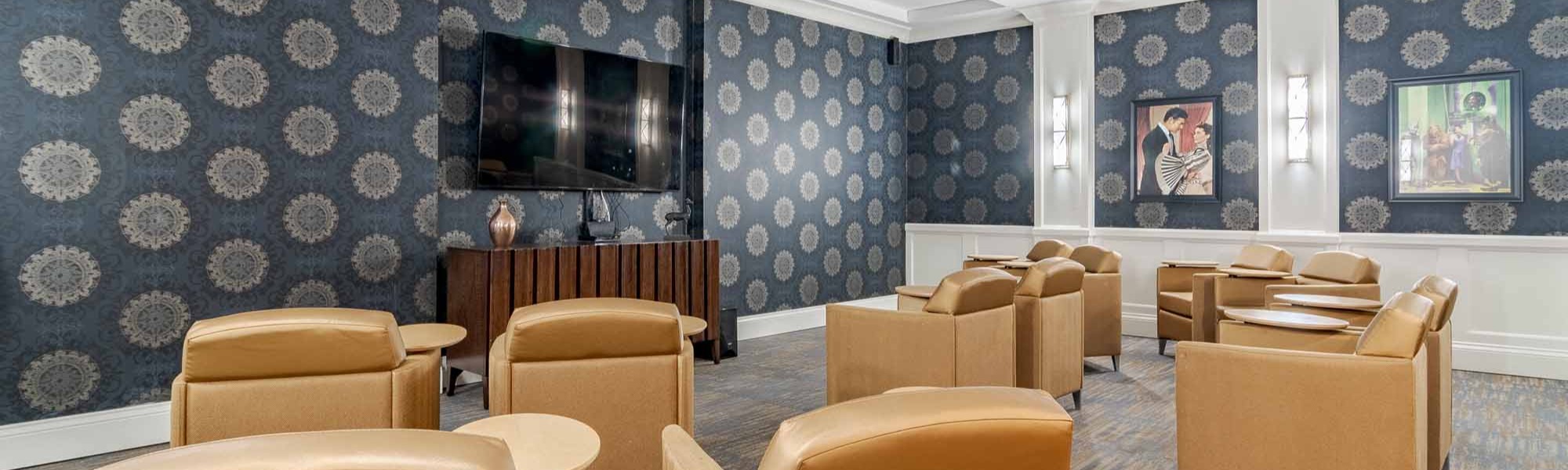 A stylish lounge area at Arbor Terrace South Forsyth features warm leather seating, a wall-mounted TV, and bold patterned wallpaper, offering a comfortable gathering space for senior living in Suwanee, GA.