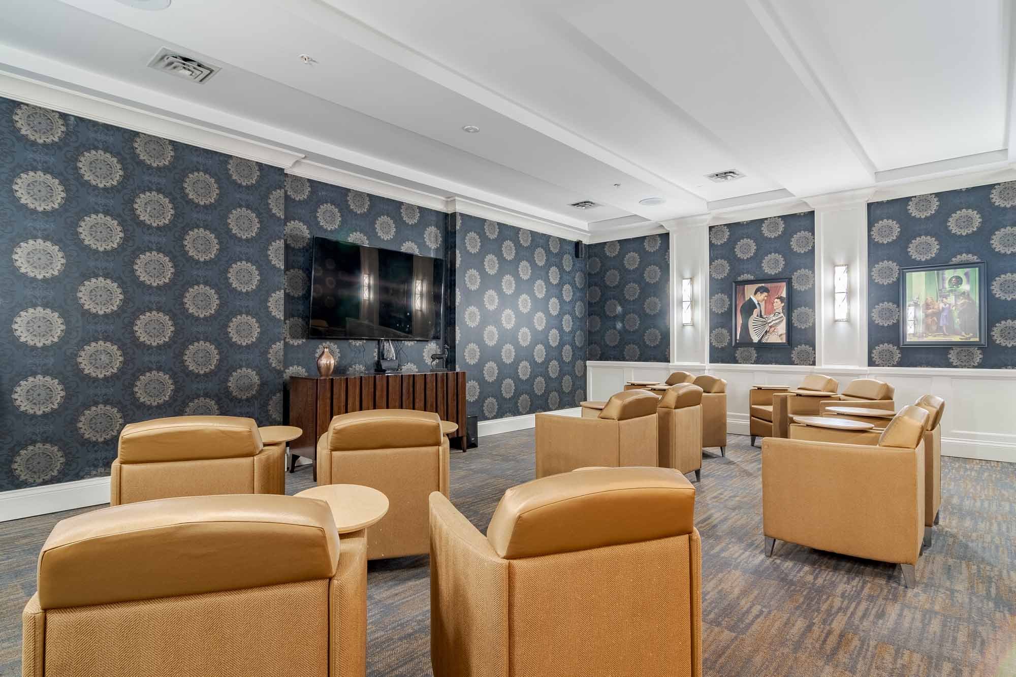 A cozy private theater room with plush tan seating and a large screen at this senior living community in Suwanee, GA.