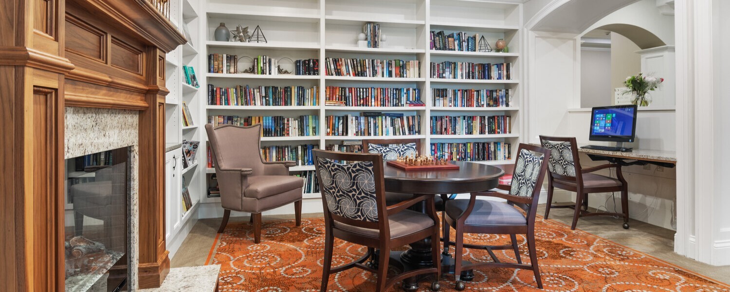 A cozy library and sitting room with built-in bookshelves, a fireplace, and comfortable seating, offering a peaceful retreat at this South Forsyth assisted living community.