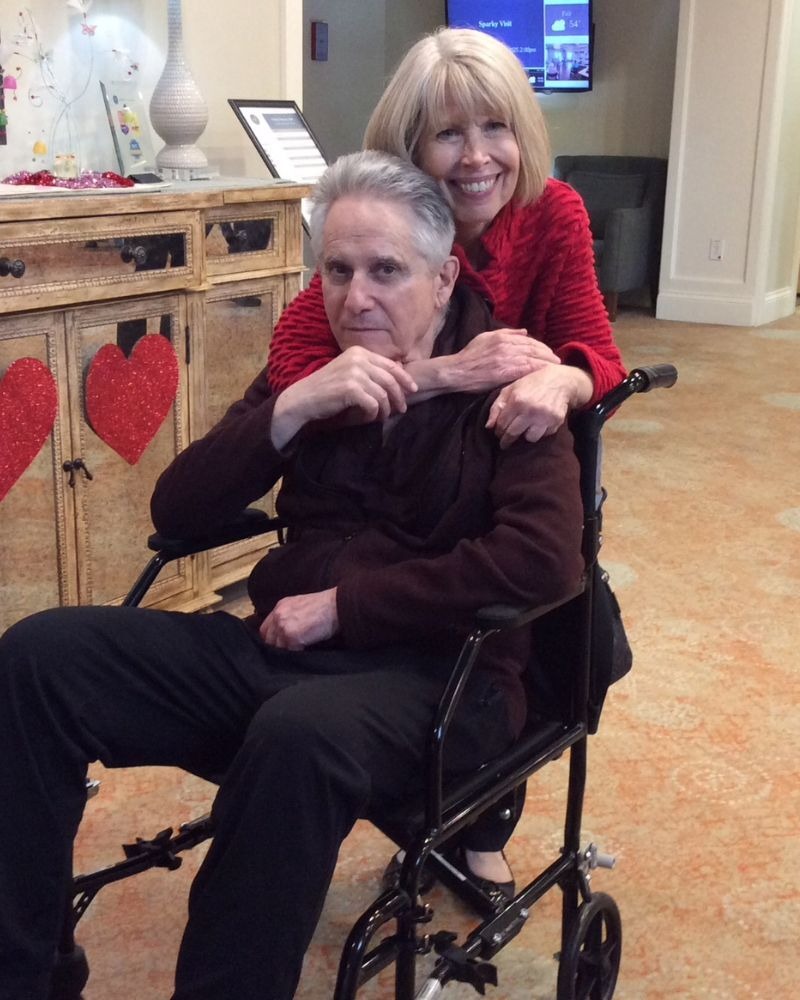 Two people share a tender moment together in the festively decorated common area during a Valentine's Day celebration at Arbor Terrace South Forsyth, a warm senior living community in Suwanee, GA.