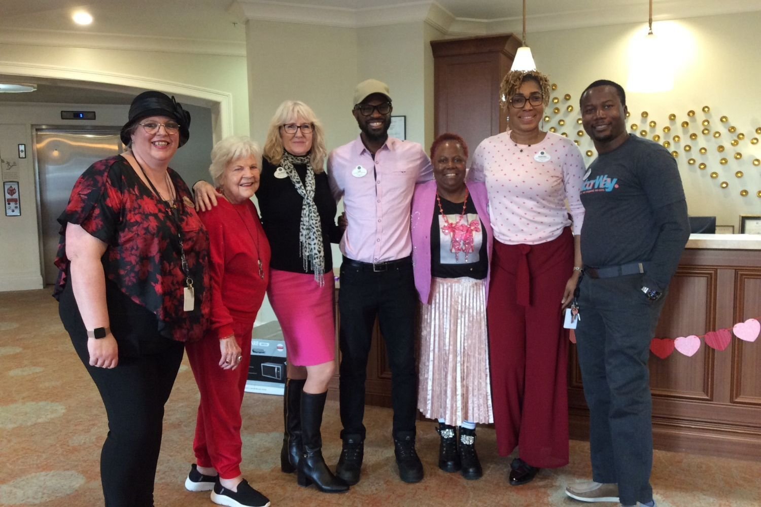 A cheerful group of residents and staff members pose together with smiles in a decorated common area at this South Forsyth assisted living community.