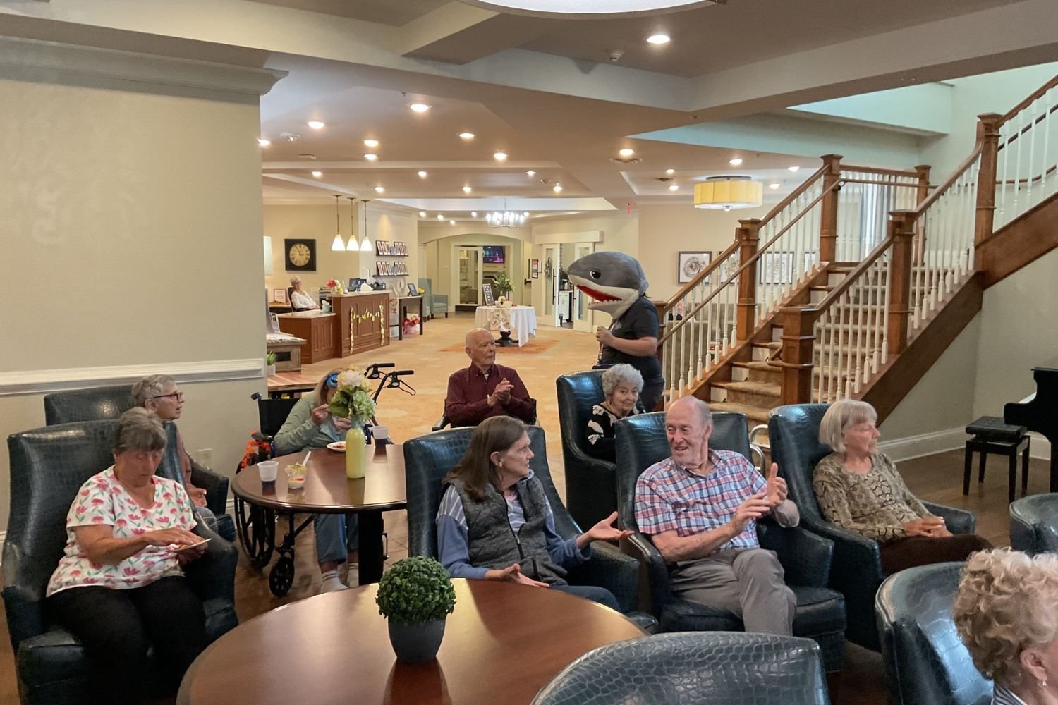 Residents relax and socialize in the spacious, staircase-flanked common area at Arbor Terrace South Forsyth, reflecting the engaged lifestyle of senior living in Suwanee, GA.