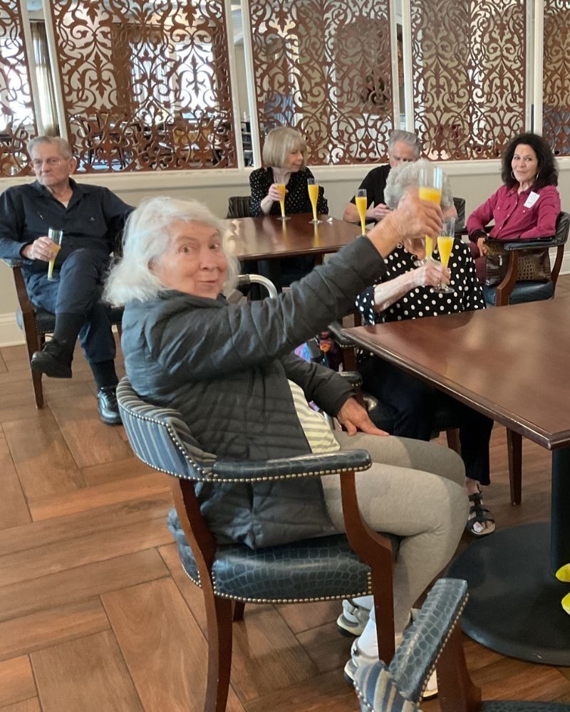 Residents raise their glasses in a cheerful toast during a social gathering at Arbor Terrace South Forsyth, celebrating the lively, connected lifestyle of senior living in Suwanee, GA.